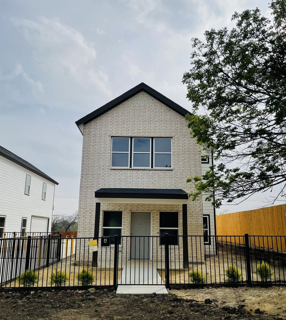 Modern white brick house with a black roof, fenced yard, and landscaped front.