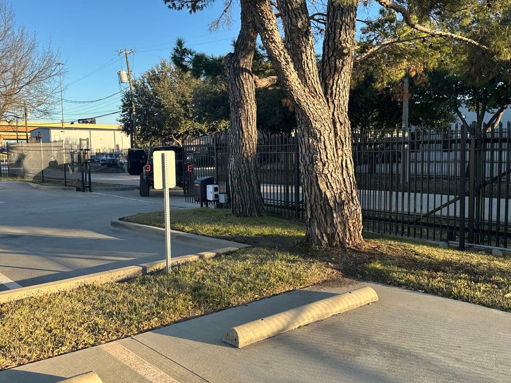 Tree-lined parking lot with a gated entrance and visible pavement bollards.