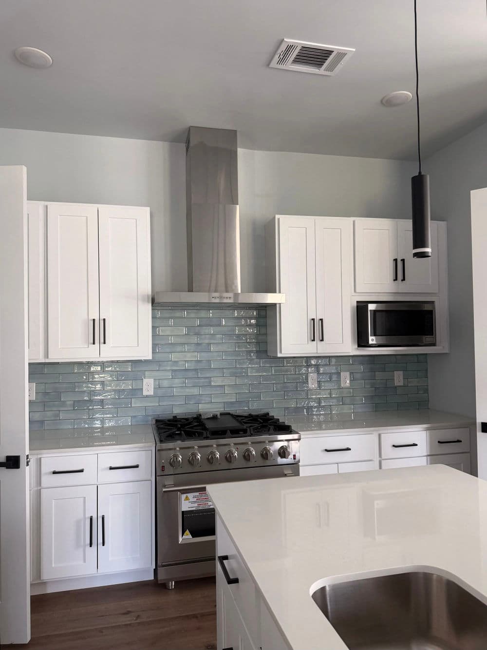 Modern kitchen with white cabinets, stainless steel appliances, and teal backsplash tiles.